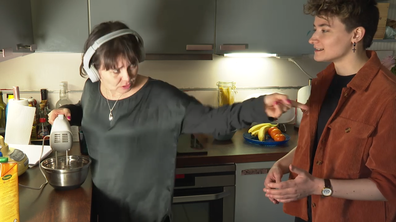kaksi nuorta naista seisovat keittiössä, toisella on sähkövatkain ja kuulokkeet